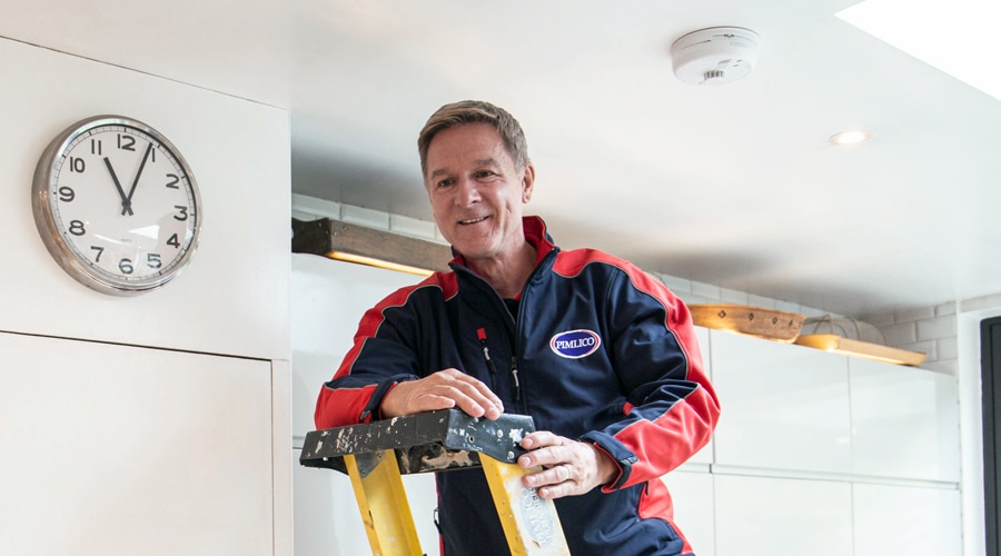 A Pimlico engineer finishes installing a new fire alarm on a client's ceiling