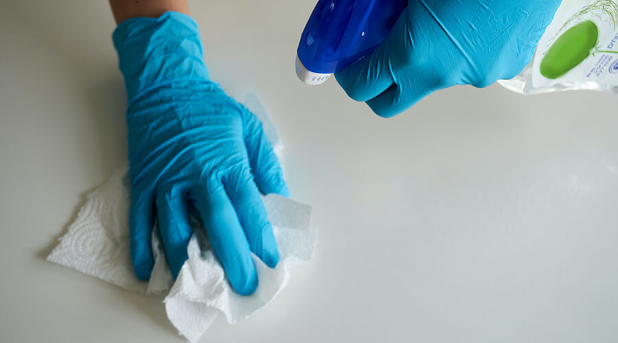 Person cleaning a worktop with a bleach product and kitchen towel while wearing blue gloves
