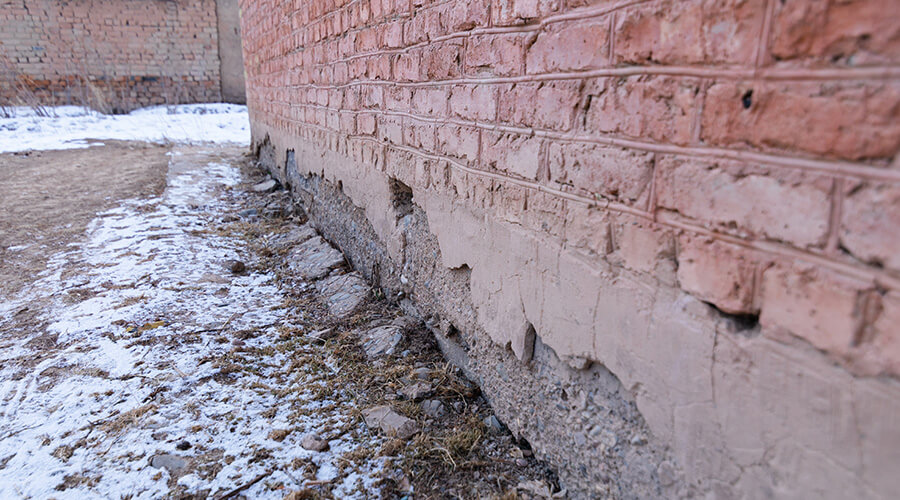 Snow and ice seeping water into the brickwork of a red brick building, with visible damage and cracked bricks