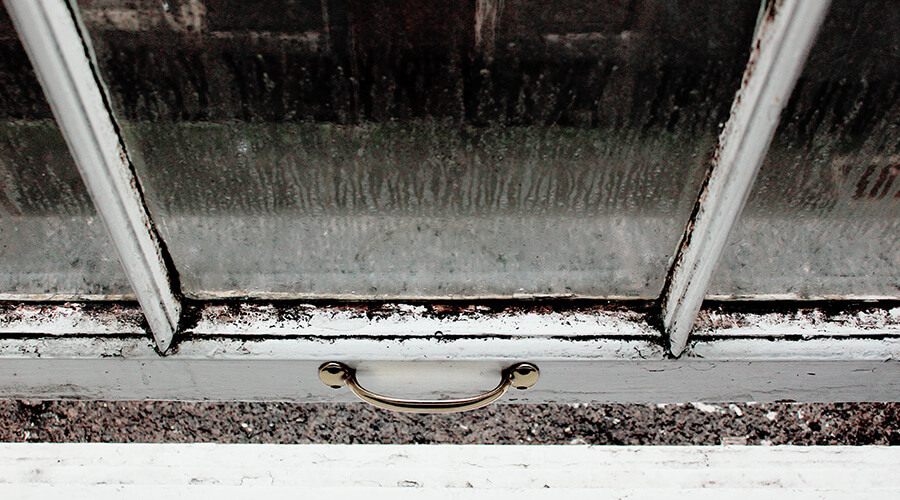 Old outdoor windowpane with condensation and mould on the glass and frame.