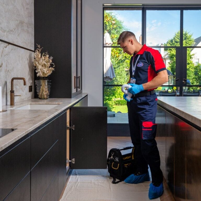A plumber standing in a kitchen with a sink pipe part in his hands