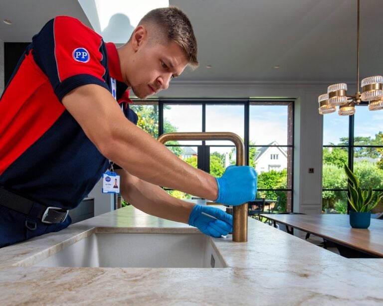 A plumber positioning and tightening a gold kitchen tap