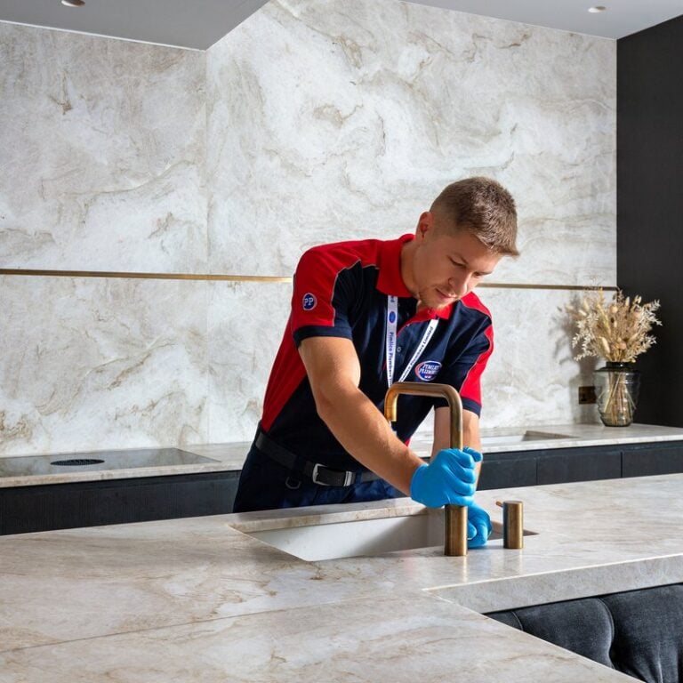 A plumber positioning a gold kitchen tap on a kitchen surface