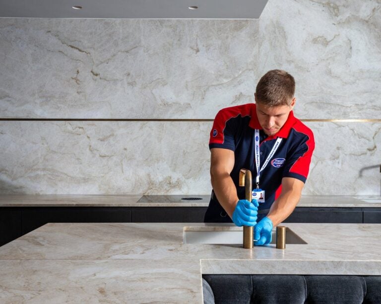 A plumber holding a gold kitchen tab on a white marbled worktop