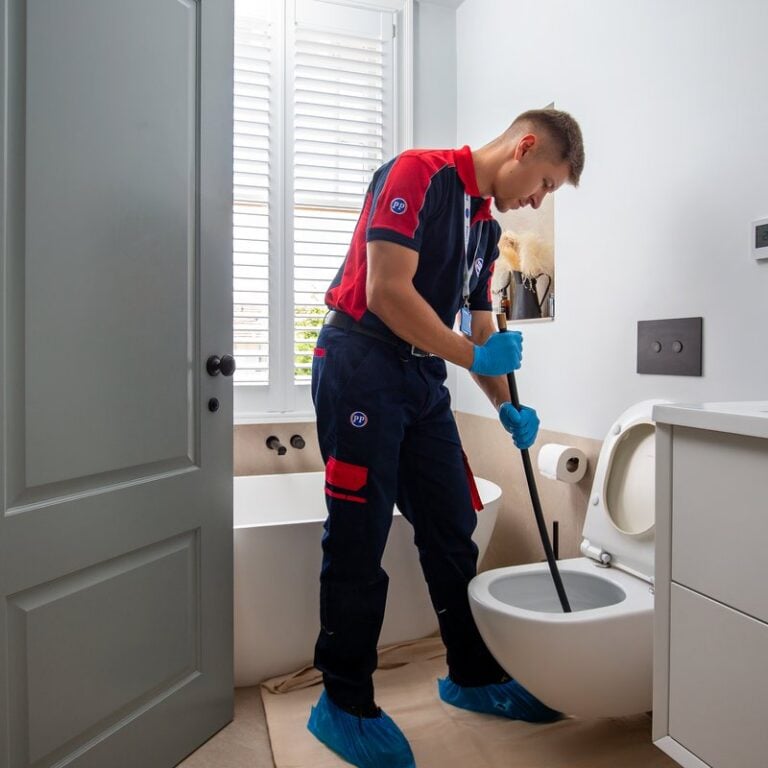 A plumber using a long tool to unblock a bathroom toilet