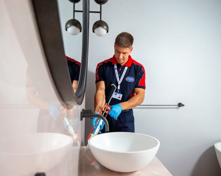 A plumber applying sealant around a bathroom sink