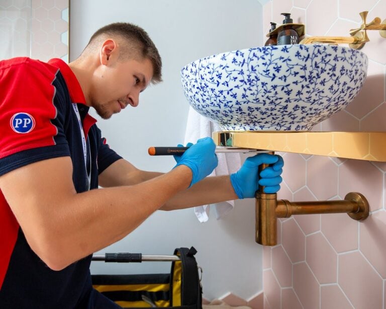 A close-up of a plumber using a tool underneath a bathroom sink