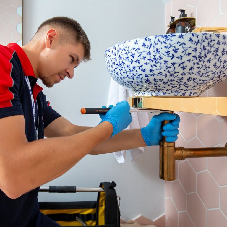 A close-up of a plumber using a tool underneath a bathroom sink