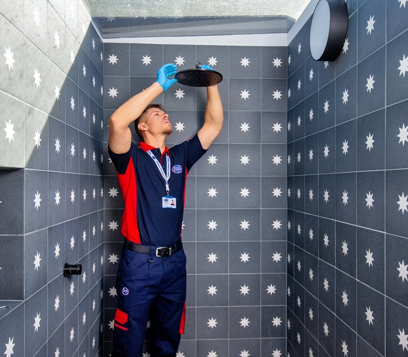 A plumber inspecting a black showerhead in a tiled shower