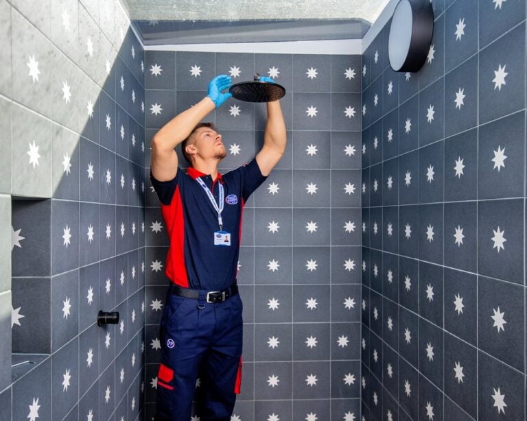 A plumber inspecting a black showerhead in a tiled shower