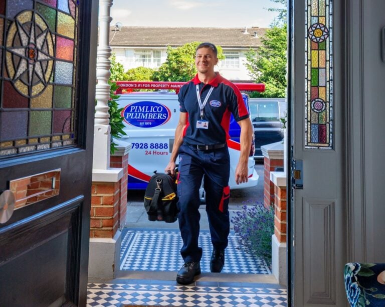 A smiling plumber walking into the front door of a home with a tool bag