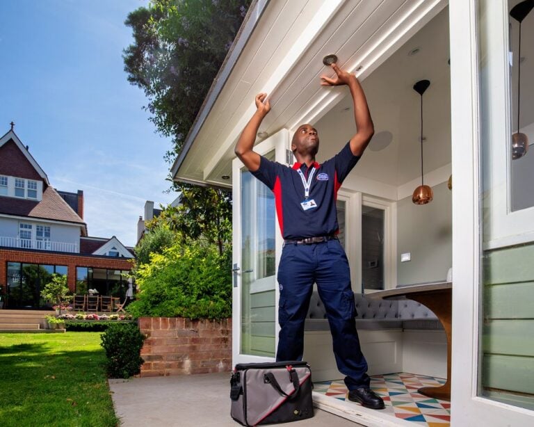 An electrician reaches up to an outdoor spotlight