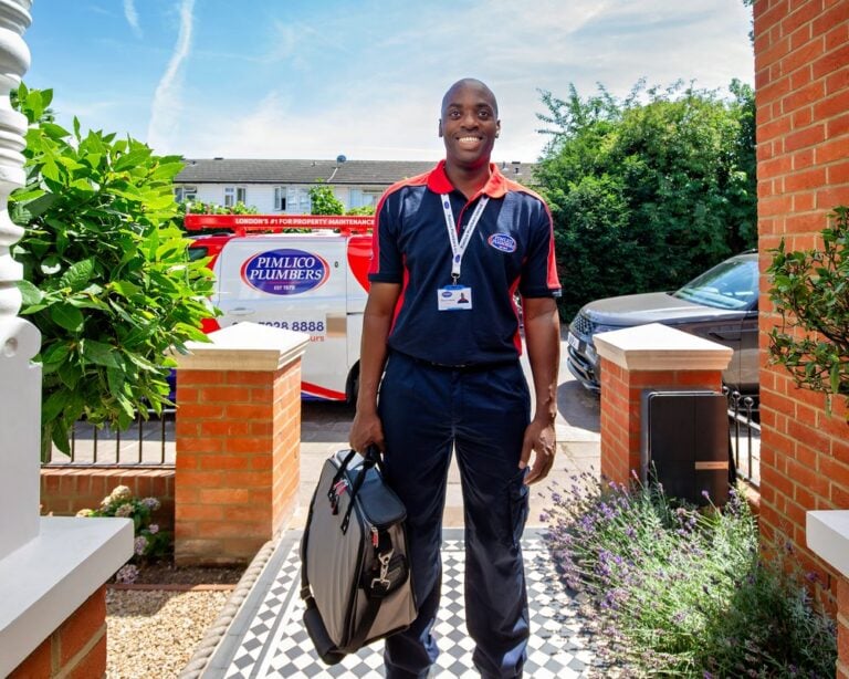 A smiling electrician stands at the front of a home with a tool bang in his hand
