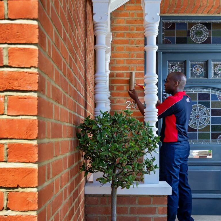 An electrician with a screwdriver tends to a front door lamp