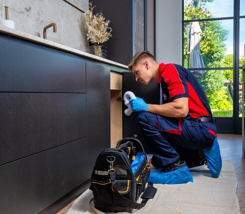 A plumber assessing a pipe underneath a kitchen sink